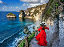 Девушка в красном летнем платье на скалистом утесе